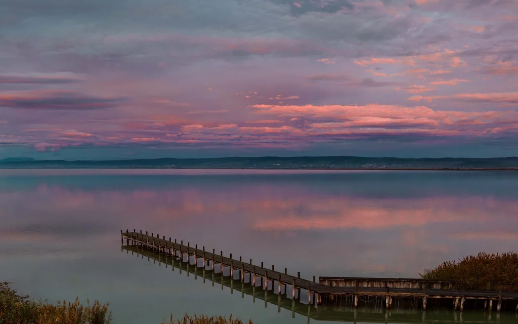 Weihnachten am See im NILS: Ruhe und Zauber Steg auf ruhigem See bei Sonnenuntergang mit rosa bewölktem Himmel