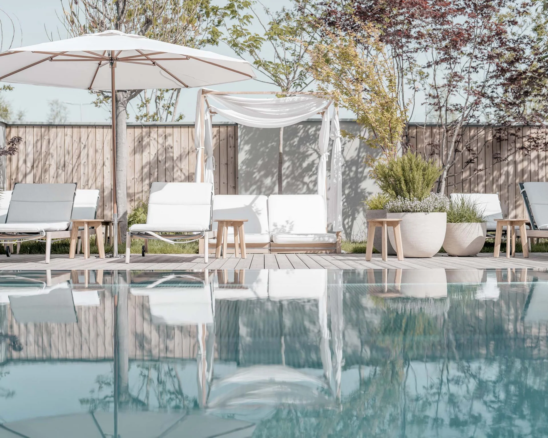 NILS am See: Impressionen eines Orts für das süße Leben Weiße Liegestühle und Sonnenschirme am Pool mit Pflanzen im Hintergrund