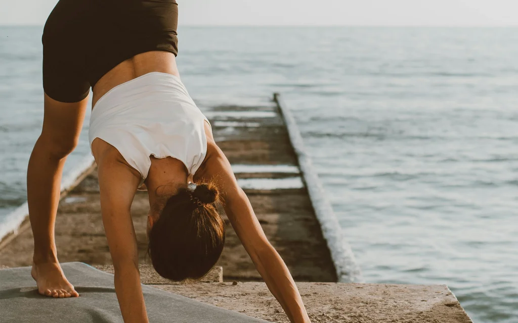 NILS am See: unser Hotel mit Yoga in Österreich Frau macht Yoga mit einem Bein auf einem Steg am Meer