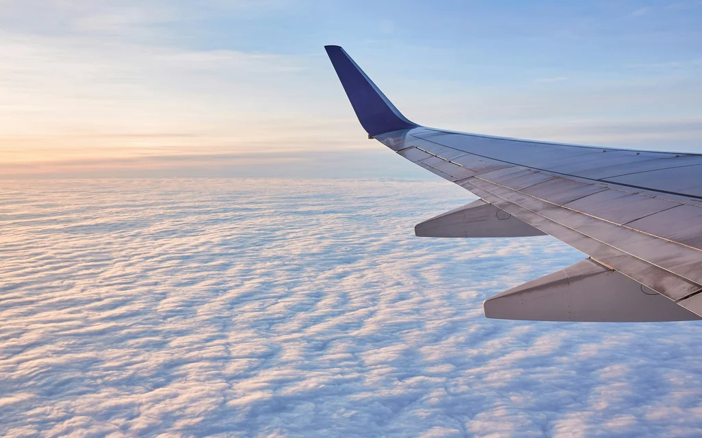 NILS am See: traumhafte Lage, unbeschwerte Anreise Flugzeugflügel über einer Wolkendecke bei Sonnenaufgang