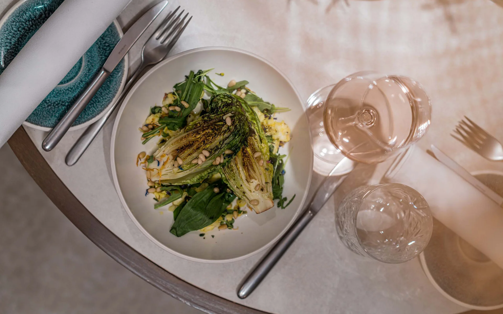 Restaurant Ankkuri am Neusiedler See Gegrillter Salat mit Pinienkernen auf weißem Teller, Besteck und Gläser auf Tisch