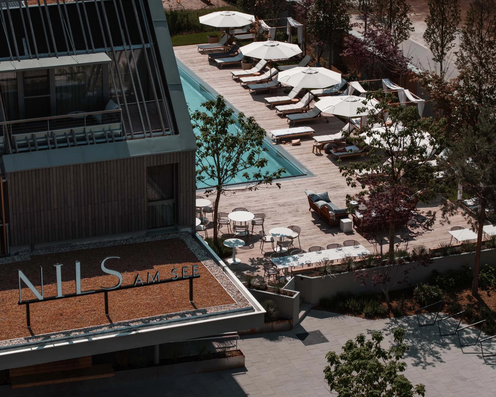 NILS am See: Impressionen eines Orts für das süße Leben Hotel mit Pool, Sonnenschirmen und Sitzecke, Schild 'NILS AM SEE'