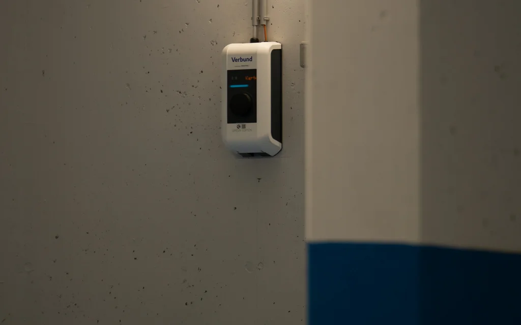 NILS am See: traumhafte Lage, unbeschwerte Anreise Wandmontierte Verbund-Ladestation in einer Parkgarage mit blauen und grauen Wänden