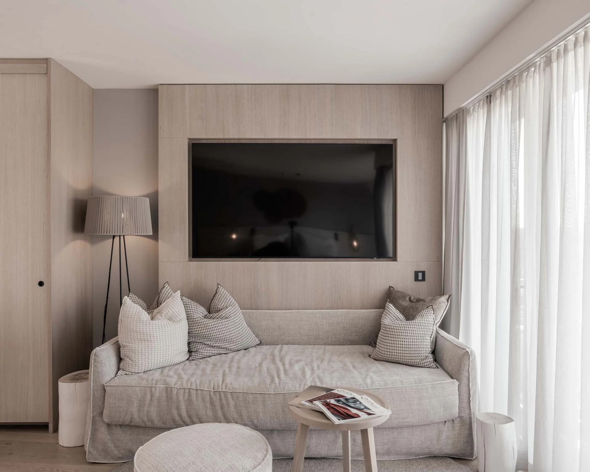 NILS am See: Impressionen eines Orts für das süße Leben Minimalistisches Wohnzimmer mit Sofa, Kissen, Stehlampe und großem Fernseher an Holzverkleidung