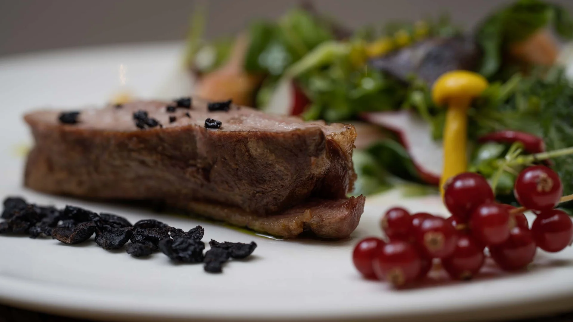 Restaurant Ankkuri am Neusiedler See Serviert Steak mit Salat, roten Johannisbeeren und schwarzen Kräutern auf weißem Teller