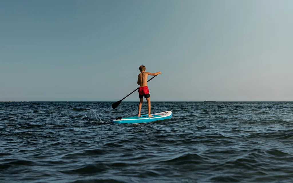 NILS am See: Wassersport am Neusiedler See Junge beim Stand-up-Paddeln auf dem offenen Meer unter klarem Himmel