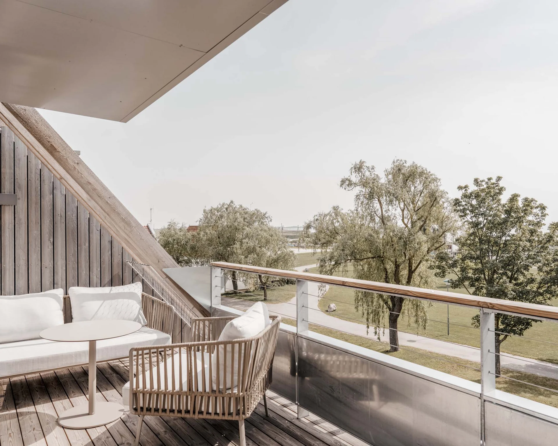 NILS am See: Impressionen eines Orts für das süße Leben Moderner Balkon mit weißen Möbeln und Blick auf grüne Bäume und Weg