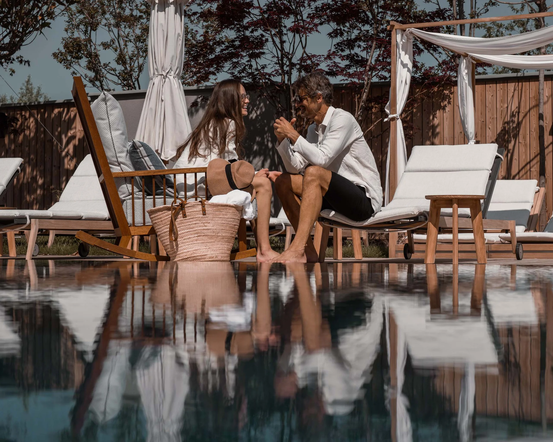 NILS am See: Impressionen eines Orts für das süße Leben Paar entspannt sich bei sonnigem Wetter neben einem Pool mit Liegestühlen