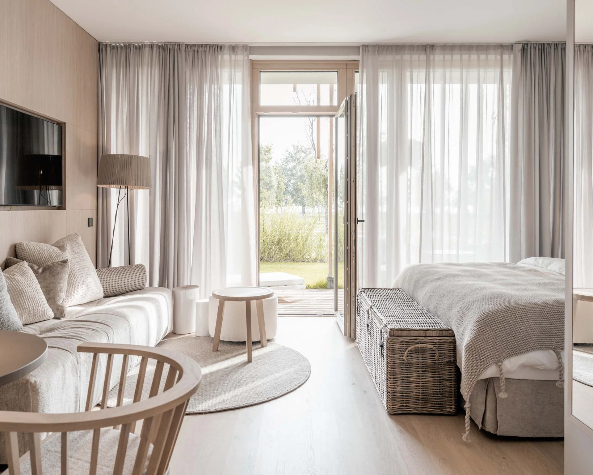NILS am See: Impressionen eines Orts für das süße Leben Helles, modernes Hotelzimmer mit Sofa, Bett, Korbtruhe und offener Tür zum Garten