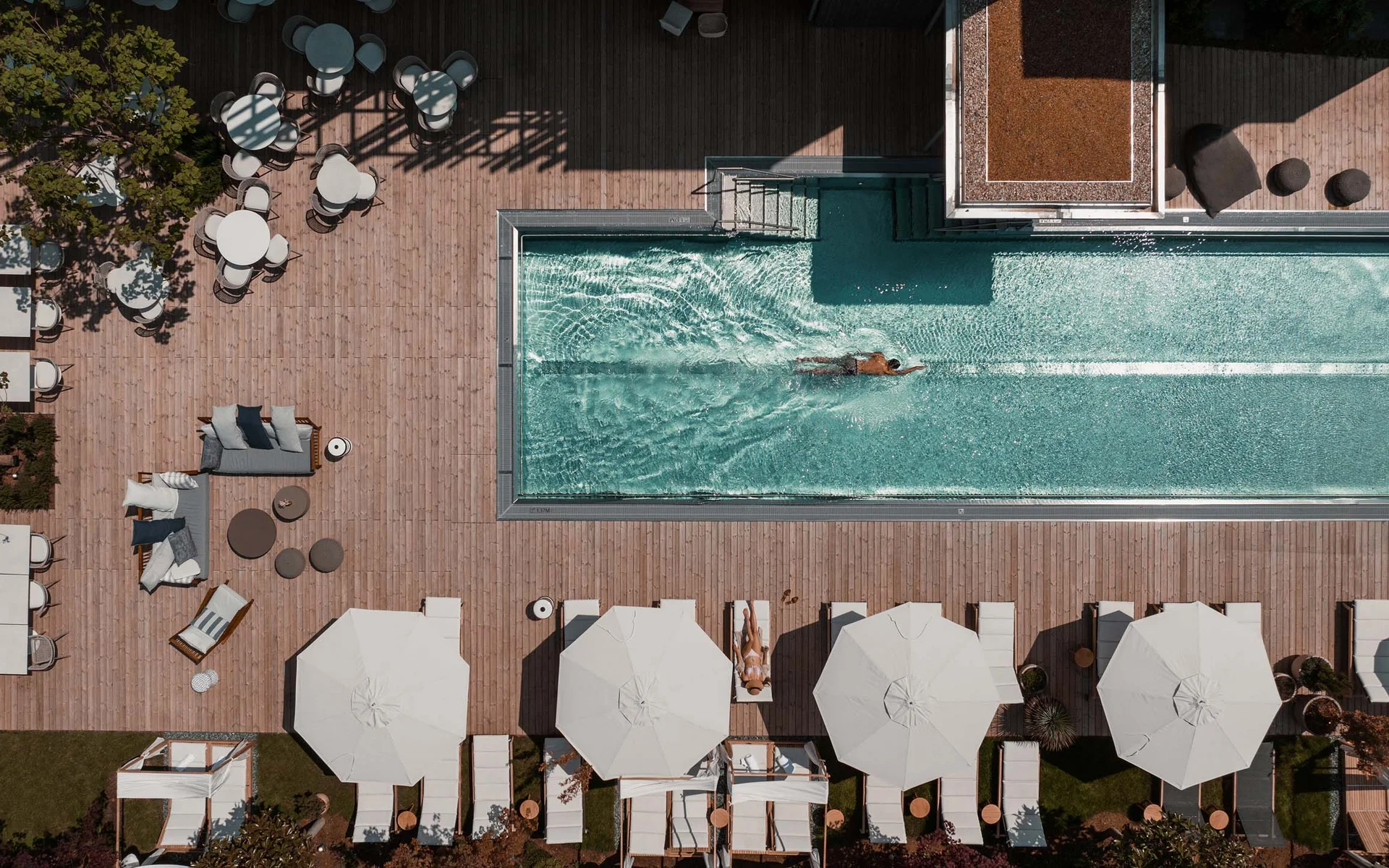 NILS am See: das Boutiquehotel am Neusiedler See Vogelperspektive auf Pool mit Schwimmer und Liegestühle mit Sonnenschirmen