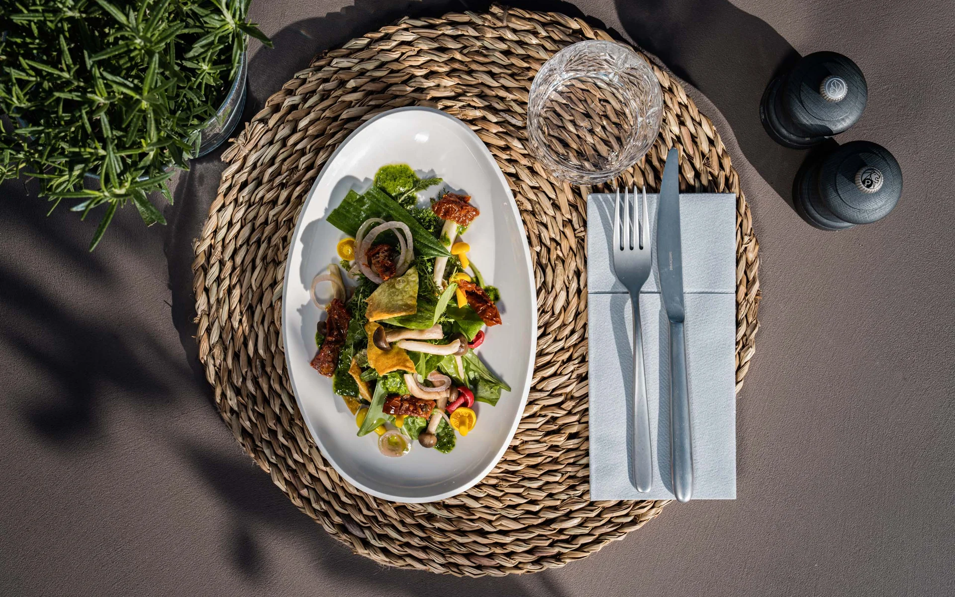 NILS am See: das Boutiquehotel am Neusiedler See Salat auf weißem Teller mit Glas, Besteck und Gewürzmühlen auf Tisch