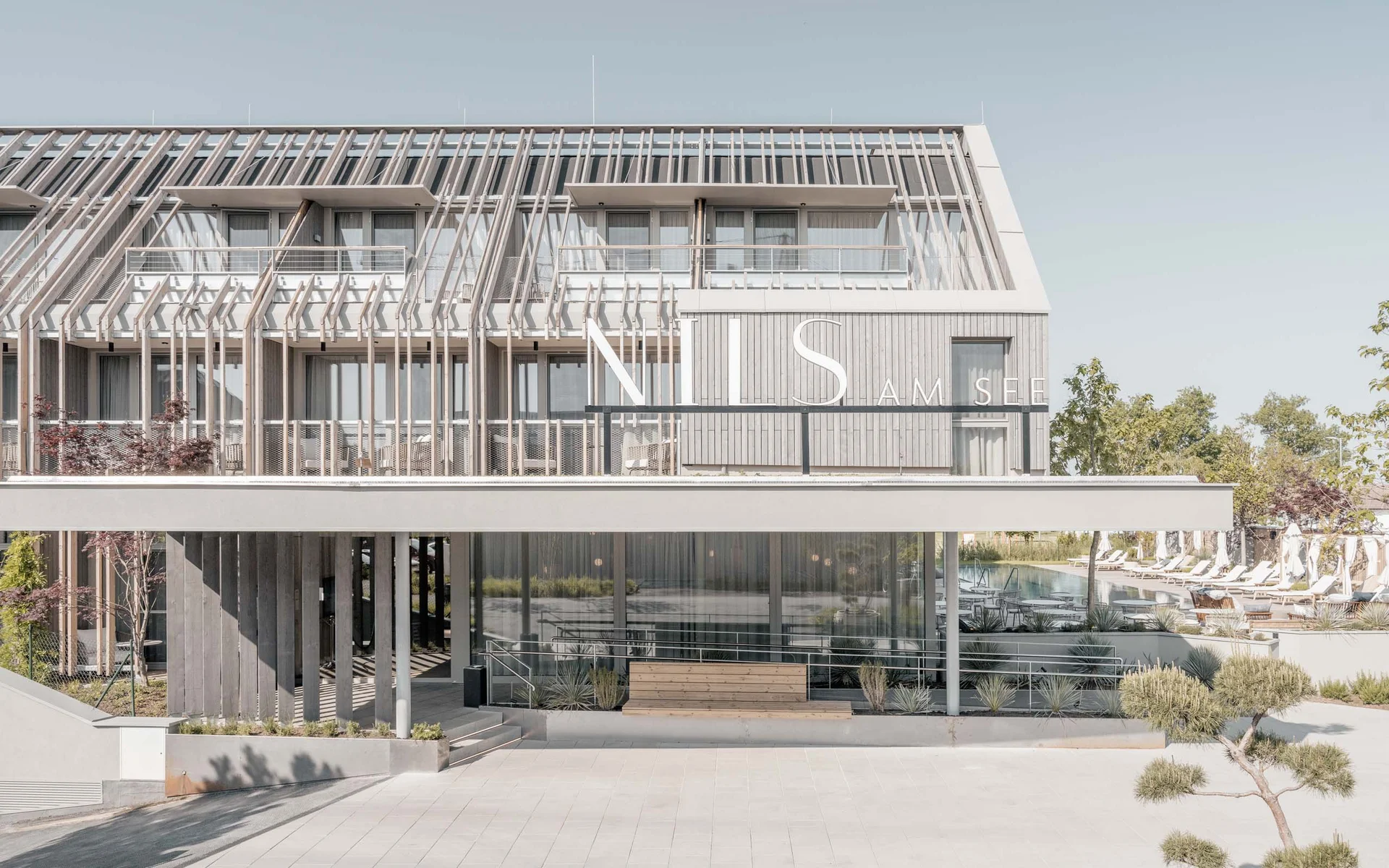 NILS am See: das Boutiquehotel am Neusiedler See Modernes Hotelgebäude mit Sonnenterrasse und Schwimmbad im Hintergrund