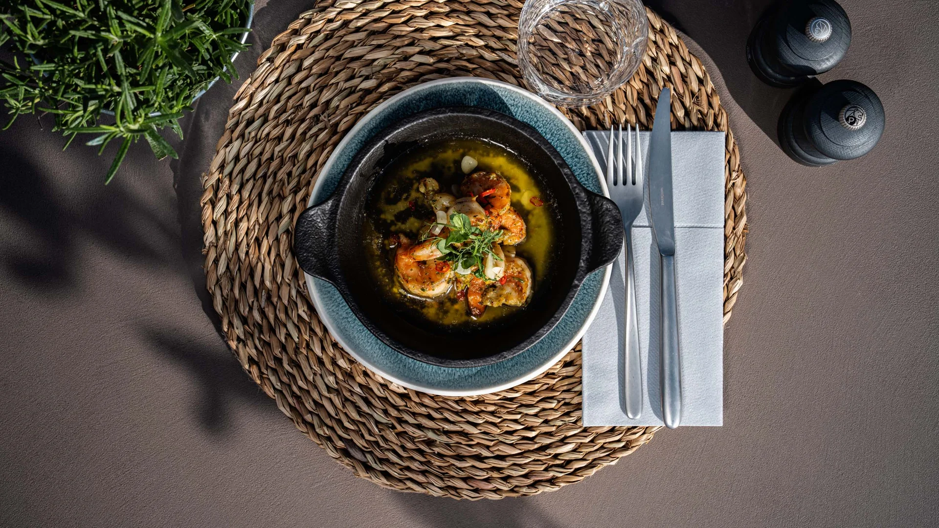 NILS am See: das Boutiquehotel am Neusiedler See Gebratene Garnelen in einer schwarzen Schale mit Besteck und Glas auf einem Tisch