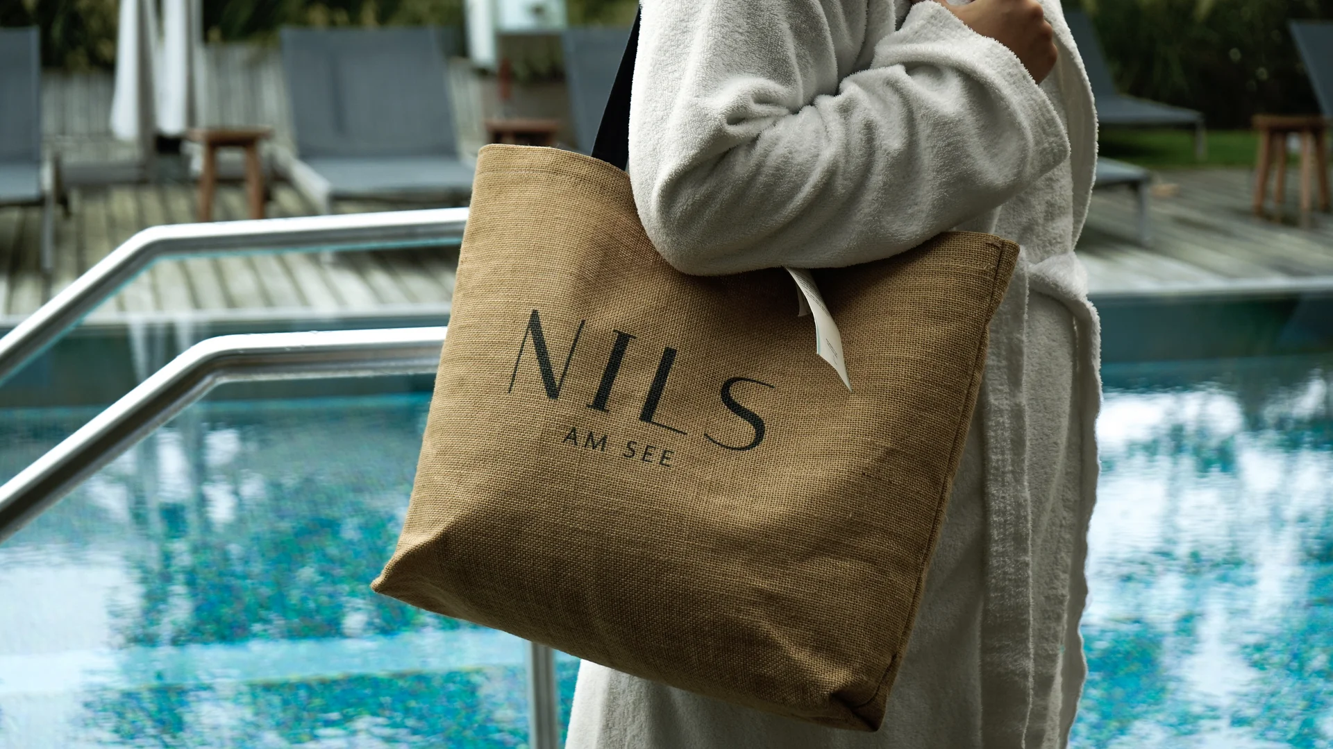 NILS am See: das Boutiquehotel am Neusiedler See Person in Bademantel trägt eine Tasche mit dem Schriftzug NILS am See