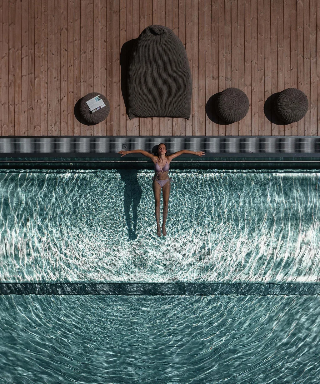 NILS am See: das Boutiquehotel am Neusiedler See Frau entspannt sich im Pool mit Sonnenliegen und Holzdeck daneben