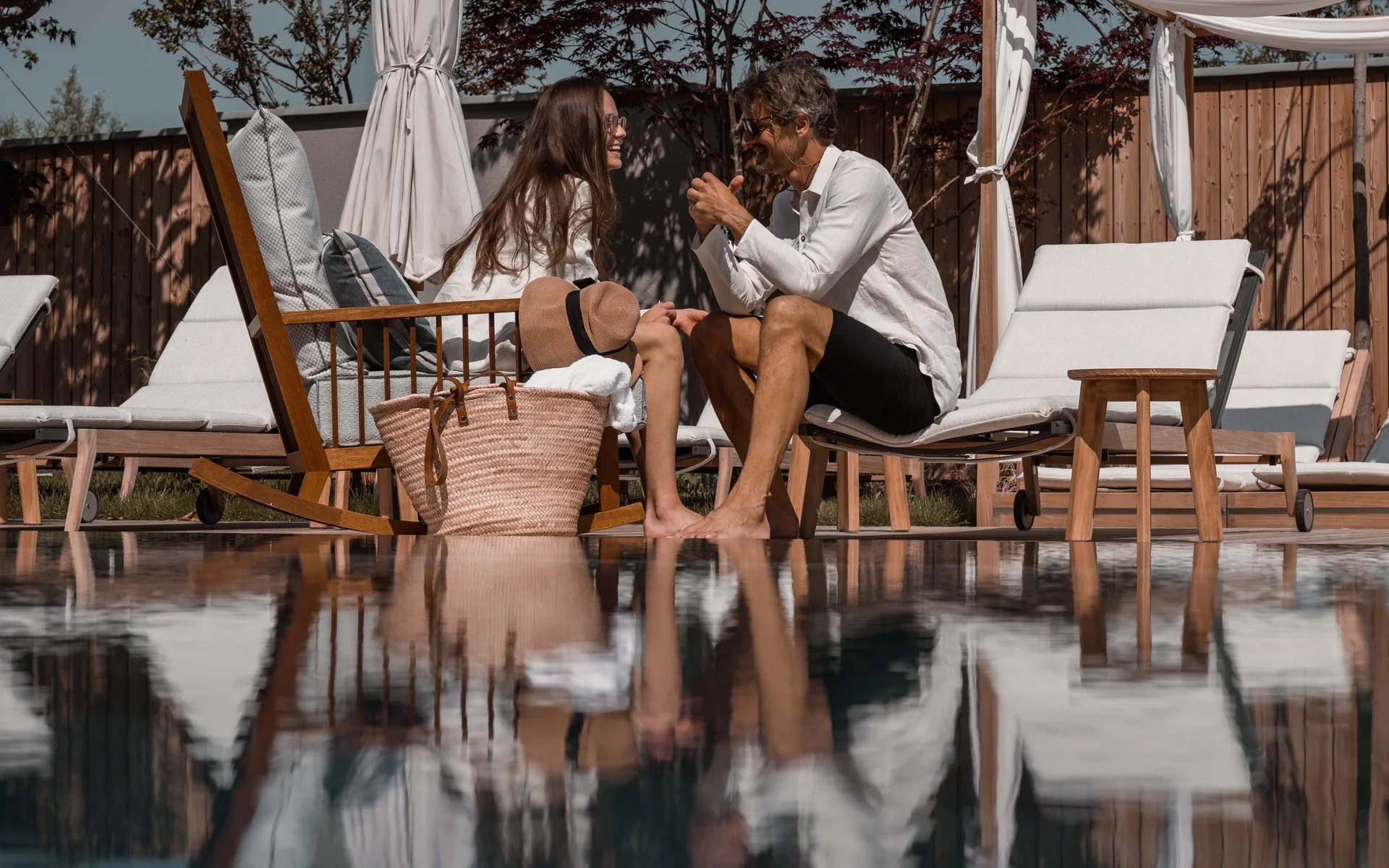 NILS am See: das Boutiquehotel am Neusiedler See Paar entspannt sich bei sonnigem Wetter neben einem Pool mit Liegestühlen