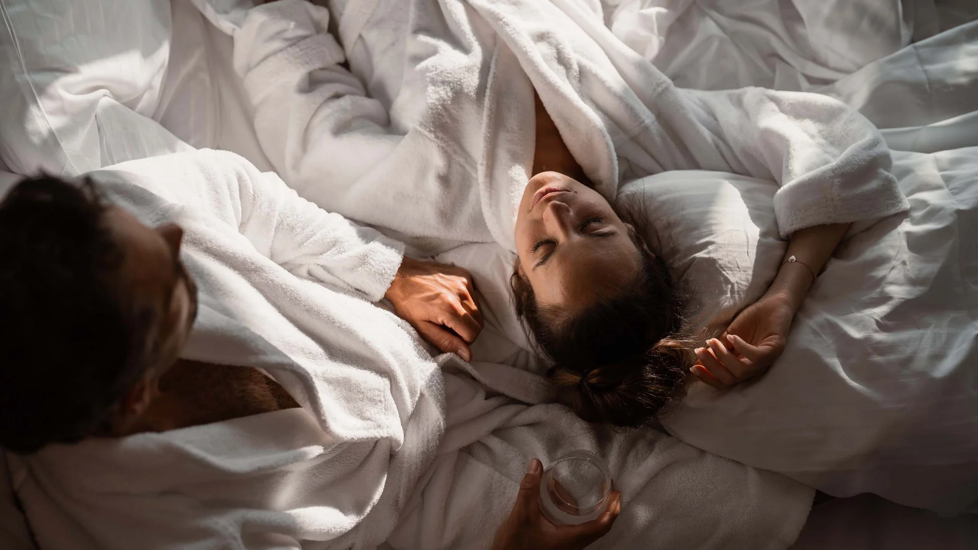 NILS am See: das Boutiquehotel am Neusiedler See Paar in weißen Bademänteln gemütlich im Bett liegend, Frau entspannt