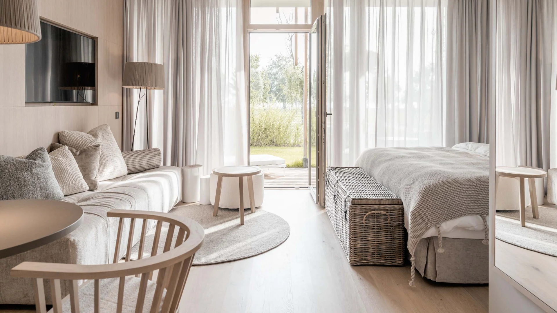 NILS am See: das Boutiquehotel am Neusiedler See Helles, modernes Hotelzimmer mit Sofa, Bett, Korbtruhe und offener Tür zum Garten